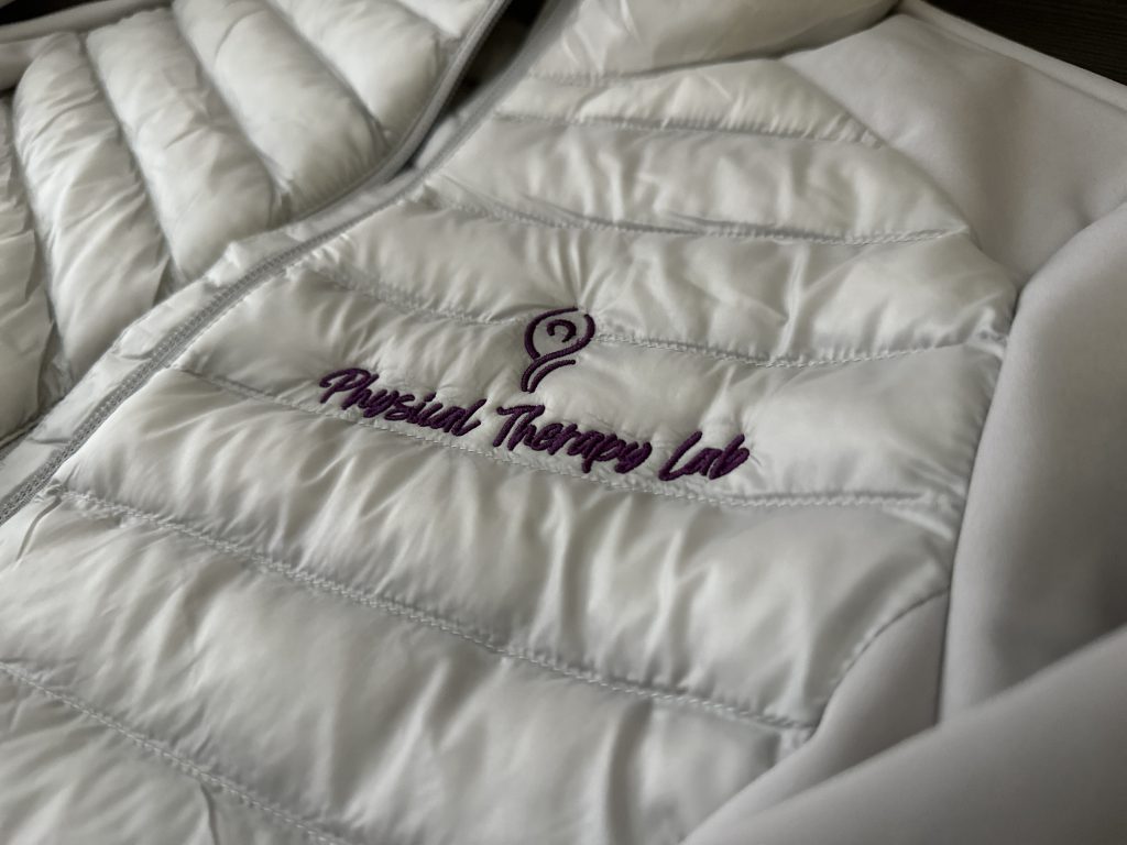 Custom physical therapy logo embroidered onto a silver puff jacket