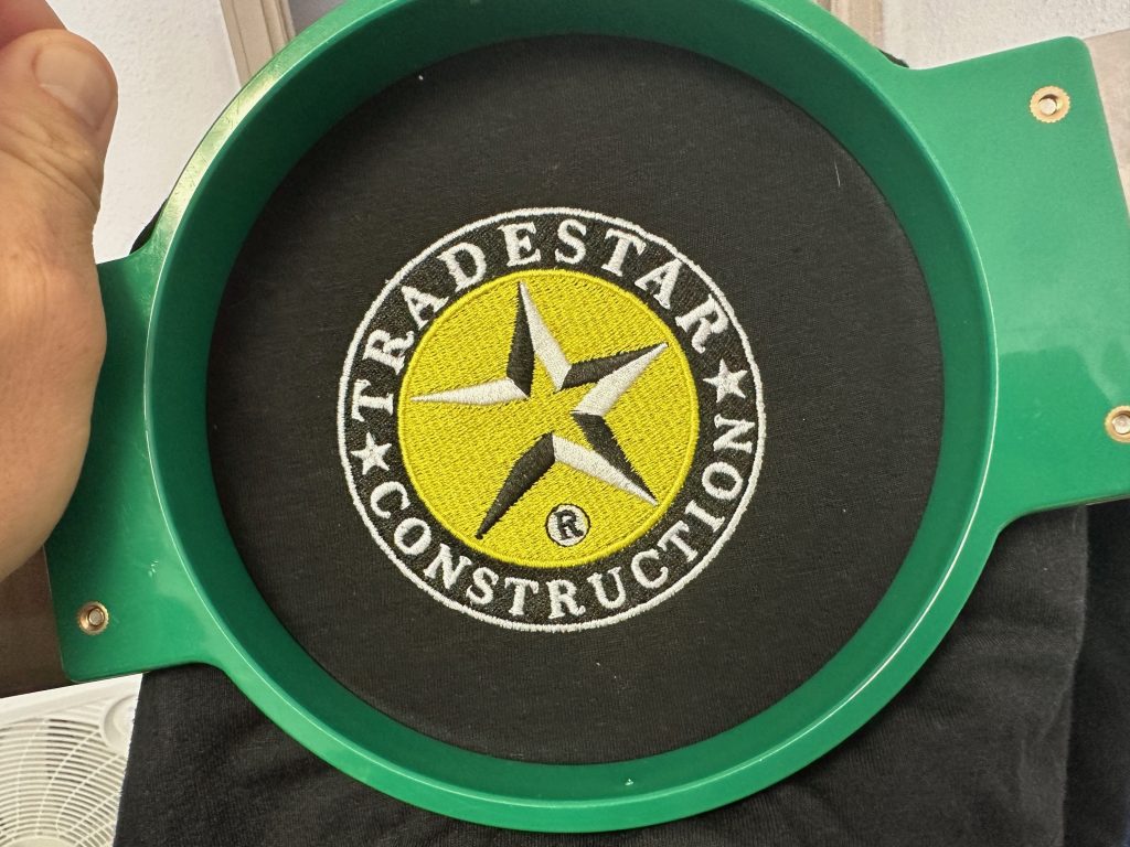 Custom embroidered logo still on the hoop at The Print Plug in Nampa